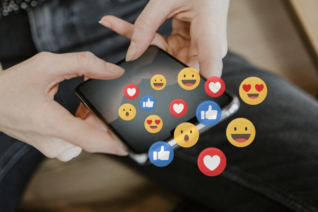 Hands holding phone with social media emoji reactions
